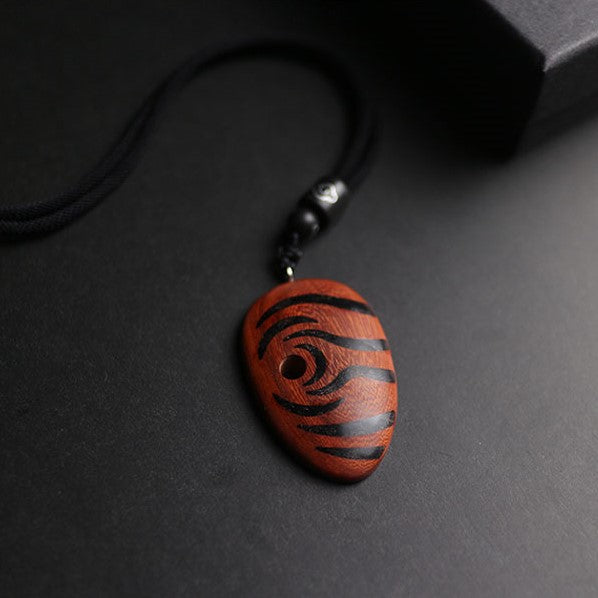 Wooden pendant with black spiral design on a dark surface